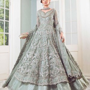 May include: A pale green formal gown with detailed silver embroidery and a layered skirt. The long-sleeved dress has a beaded neckline and a matching shawl. A small, cream-coloured clutch is held.