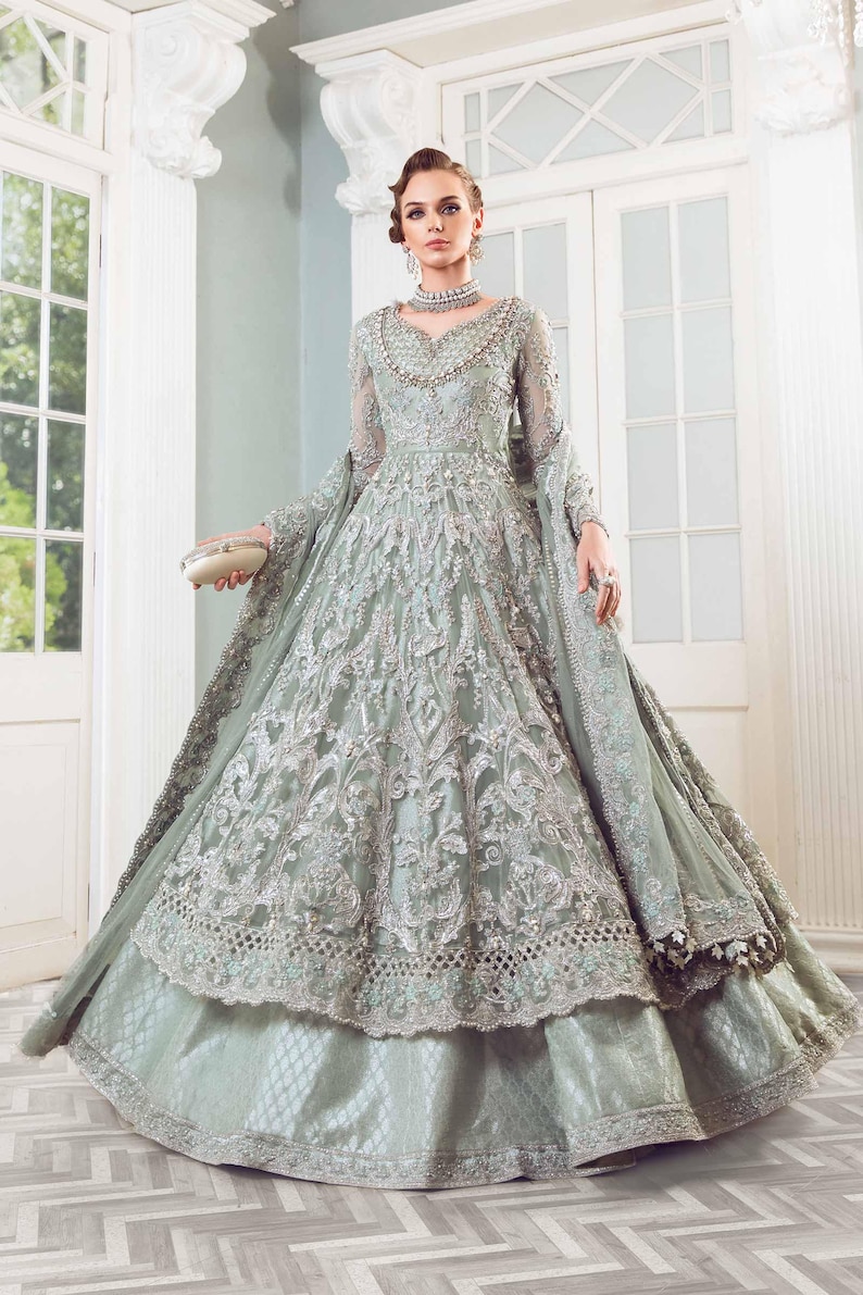 May include: A pale green formal gown with detailed silver embroidery and a layered skirt. The long-sleeved dress has a beaded neckline and a matching shawl. A small, cream-coloured clutch is held.