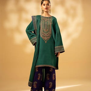 May include: A teal green tunic and matching scarf with intricate gold embroidery around the neckline and sleeves. The outfit is paired with wide-leg, dark purple pants featuring a paisley pattern with red and gold accents. The ensemble is a traditional style.