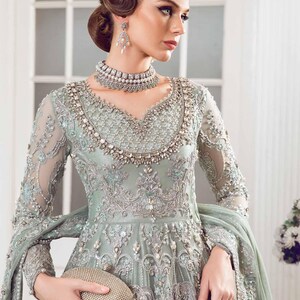 May include: A pale green formal gown with detailed silver embroidery and beading. The long-sleeved dress has a V-neck and a flowing skirt. A matching clutch and jewellery complete the elegant ensemble.