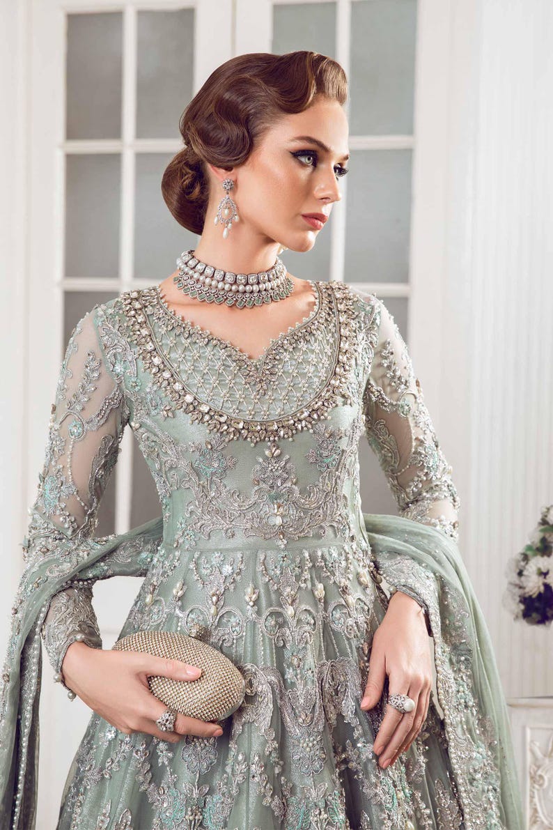 May include: A pale green formal gown with detailed silver embroidery and beading. The long-sleeved dress has a V-neck and a flowing skirt. A matching clutch and jewellery complete the elegant ensemble.