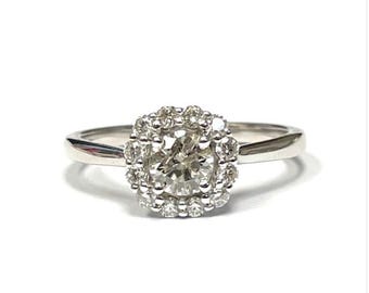 May include: A silver ring with a round diamond center stone surrounded by a halo of smaller diamonds.