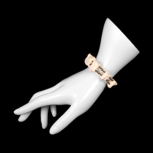 May include: A cream-colored bracelet with irregular, organic-shaped beads and small, bronze-colored beads. The bracelet is displayed on a white mannequin hand against a black background. The bracelet appears to be made of natural materials.