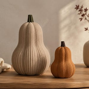 May include: Two decorative gourd-shaped pumpkins with a ribbed texture. The larger pumpkin is a light cream colour with a dark green stem, while the smaller pumpkin is a warm orange colour with a dark brown stem, both featuring vertical ridges.