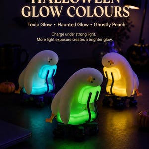 K&ouml;nnte beinhalten: Drei wei&szlig;e, entenartige Figuren auf Miniatur-B&uuml;rost&uuml;hlen, die in Blau, Gr&uuml;n und Gelb leuchten. Der Text lautet: HALLOWEEN GLOW COLOURS, Toxic Glow, Haunted Glow, Ghostly Peach, Charge under strong light. Aufladung durch starkes Licht.