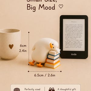 Puede incluir: Una figura de pato blanco descansando sobre una pila de cuatro libros, junto a un lector electr&oacute;nico Kindle y una taza beige con un coraz&oacute;n. El pato mide 6 cm de alto y 6,5 cm de ancho. El texto dice Small Size, Big Mood.