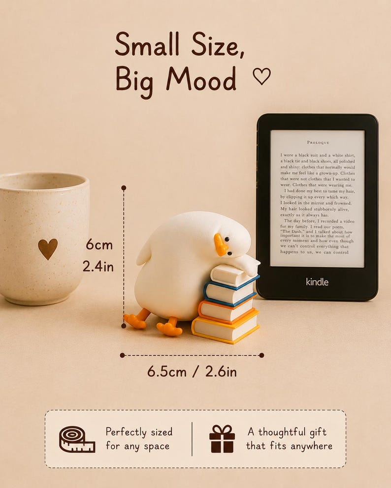 Puede incluir: Una figura de pato blanco descansando sobre una pila de cuatro libros, junto a un lector electr&oacute;nico Kindle y una taza beige con un coraz&oacute;n. El pato mide 6 cm de alto y 6,5 cm de ancho. El texto dice Small Size, Big Mood.