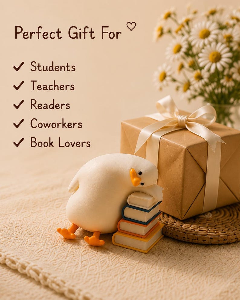 Puede incluir: Una figura de pato blanco descansando sobre una pila de tres libros peque&ntilde;os, junto a una caja de regalo marr&oacute;n atada con una cinta color crema. El texto dice: Perfect Gift For Students, Teachers, Readers, Coworkers, Book Lovers, con marcas.