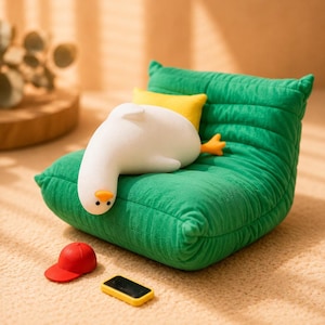 May include: A plush green tufted chair with a white goose figure resting on it, accompanied by a small yellow pillow. A tiny red baseball cap and a small yellow rectangular object are placed in front of the chair on the floor surface.