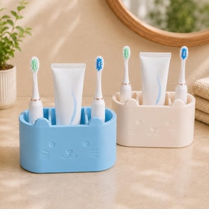 Può includere: Due portaspazzolini ovali, uno azzurro e uno beige, entrambi caratterizzati da un design a forma di muso di gatto con orecchie, occhi e baffi. Ogni supporto contiene due spazzolini elettrici bianchi e un tubetto di dentifricio.
