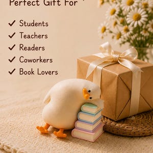 Puede incluir: Una figura de pato color crema descansando sobre una pila de cuatro libros de tonos pastel junto a una caja de regalo marr&oacute;n atada con una cinta crema. El texto dice: Perfect Gift For Students, Teachers, Readers, Coworkers, Book Lovers, con un coraz&oacute;n.