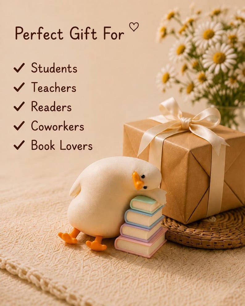 Puede incluir: Una figura de pato color crema descansando sobre una pila de cuatro libros de tonos pastel junto a una caja de regalo marr&oacute;n atada con una cinta crema. El texto dice: Perfect Gift For Students, Teachers, Readers, Coworkers, Book Lovers, con un coraz&oacute;n.