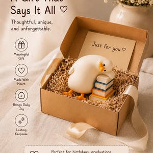 Puede incluir: Una caja de regalo de cart&oacute;n marr&oacute;n rellena de papel triturado, que contiene una figura de pato blanco descansando sobre una pila de cuatro libros coloridos. Una tarjeta interior dice Just for you. La tapa muestra el texto A Gift That Says It All.