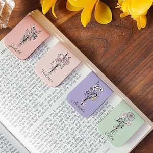 Può includere: Quattro segnalibri floreali dai colori pastello, ognuno con un nome diverso: Judith, Victoria, Amanda e Chloe. Ogni segnalibro presenta un'illustrazione floreale ed è posto su un libro aperto con testo.