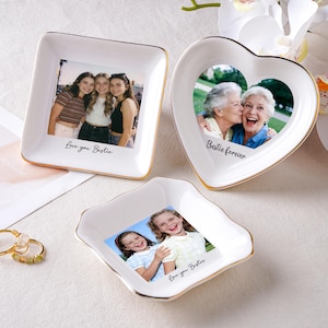 May include: Three white ceramic trinket dishes with gold rims, each featuring a photograph. One is square, one heart-shaped, and one irregularly shaped. The square dish has the text "Love you Bestie". The heart-shaped dish has the text "Bestie forever".