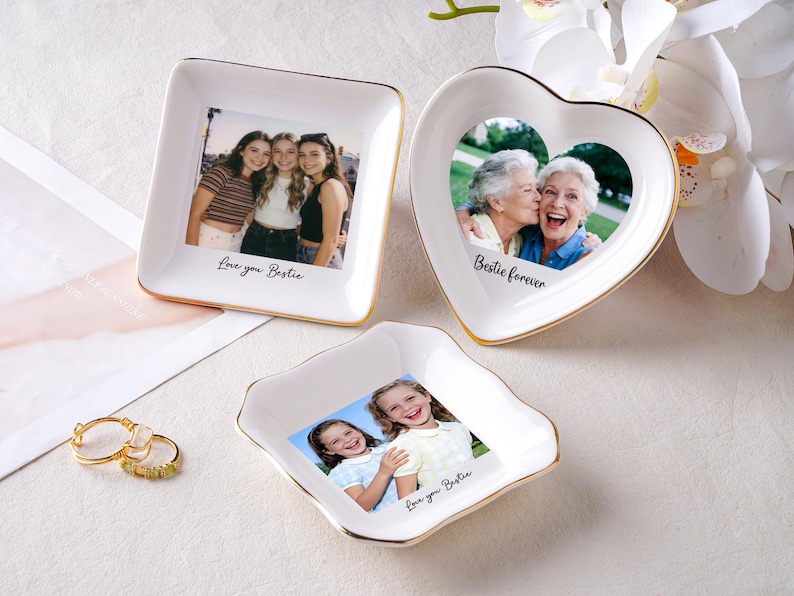 May include: Three white ceramic trinket dishes with gold rims, each featuring a photograph. One is square, one heart-shaped, and one irregularly shaped. The square dish has the text "Love you Bestie". The heart-shaped dish has the text "Bestie forever".