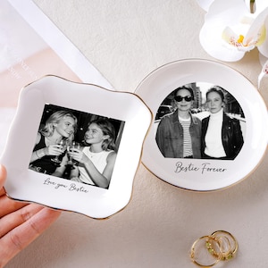 May include: Two white ceramic trinket dishes with gold rims. One is square with a photo of two women and the text "Love you Bestie." The other is round with a photo of two women and the text "Bestie Forever."