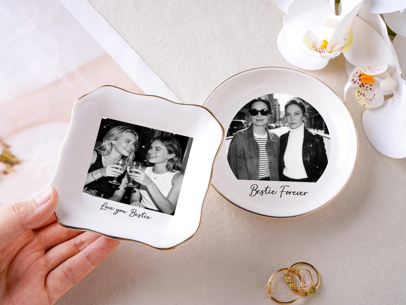 May include: Two white ceramic trinket dishes with gold rims. One is square with a photo of two women and the text "Love you Bestie." The other is round with a photo of two women and the text "Bestie Forever."