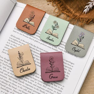 Puede incluir: Cinco marcadores magn&eacute;ticos de cuero en varios colores, cada uno con un dise&ntilde;o floral y un nombre: Bella, Amelia, Crystal, Charlie y Grace. Los marcadores est&aacute;n sobre un libro abierto.
