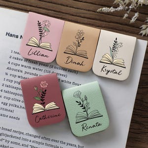 Puede incluir: Cinco marcadores rectangulares en tonos pastel, cada uno con un dise&ntilde;o floral sobre una ilustraci&oacute;n de libro abierto. Los nombres est&aacute;n escritos debajo del libro. Los marcadores est&aacute;n sobre una p&aacute;gina de libro de cocina.