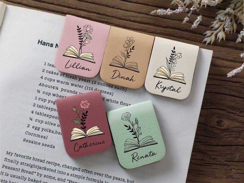 Puede incluir: Cinco marcadores rectangulares en tonos pastel, cada uno con un dise&ntilde;o floral sobre una ilustraci&oacute;n de libro abierto. Los nombres est&aacute;n escritos debajo del libro. Los marcadores est&aacute;n sobre una p&aacute;gina de libro de cocina.
