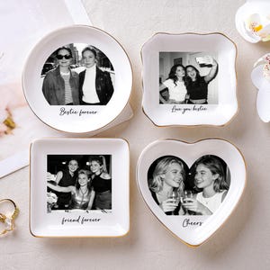 May include: Four white ceramic trinket dishes with gold rims, each featuring a black and white photo and a message. The shapes include a circle, a square, a heart, and a uniquely shaped square. Text includes "Bestie forever", "Love you bestie", "friend forever", and "Cheers".