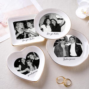 May include: Four white ceramic trinket dishes in various shapes: square, round, and heart-shaped. Each dish features a black and white photo and gold trim. Text includes "Love you Bestie" and "Bestie forever".