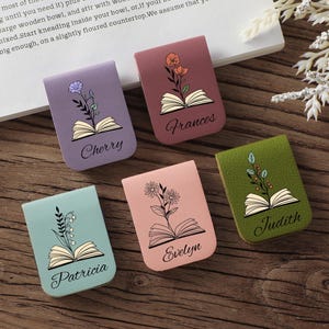 Puede incluir: Cinco marcadores magn&eacute;ticos coloridos con dise&ntilde;os florales y nombres: Cherry, Frances, Patricia, Evelyn y Judith. Cada marcador presenta una ilustraci&oacute;n de libro abierto. Los marcadores est&aacute;n sobre una superficie de madera.