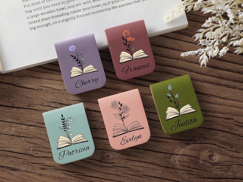 Puede incluir: Cinco marcadores magn&eacute;ticos coloridos con dise&ntilde;os florales y nombres: Cherry, Frances, Patricia, Evelyn y Judith. Cada marcador presenta una ilustraci&oacute;n de libro abierto. Los marcadores est&aacute;n sobre una superficie de madera.