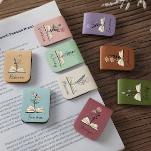 Puede incluir: Una colección de sujetapáginas de cuero de colores, cada uno con un diseño floral y un nombre. Los sujetapáginas, en varios colores como rosa y verde, están colocados en una página de recetas.