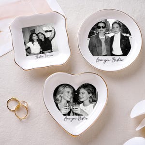 May include: Three white ceramic trinket dishes with gold rims, each featuring a black and white photo. One is square, one round, and one heart-shaped. Text on the dishes reads "Bestie Forever" and "Love you Bestie". Gold rings are next to the dishes.