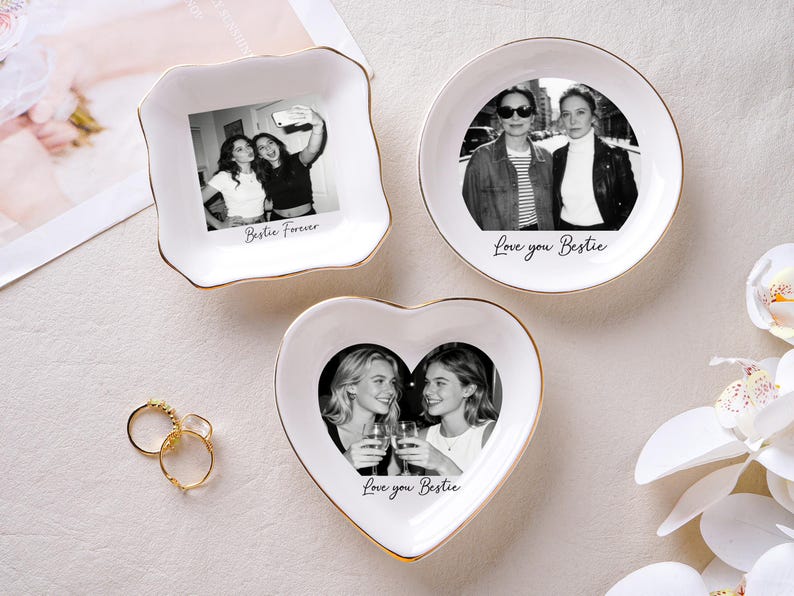 May include: Three white ceramic trinket dishes with gold rims, each featuring a black and white photo. One is square, one round, and one heart-shaped. Text on the dishes reads "Bestie Forever" and "Love you Bestie". Gold rings are next to the dishes.