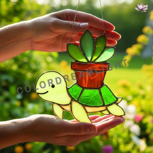 May include: Stained glass turtle with a potted plant design. The turtle is light green with a smiling face and a green shell. The plant pot is brown, and the plant has green leaves. The words "COLORDREAMLIGHT" are visible.