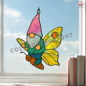 May include: Stained glass butterfly gnome with a pink hat, blue and green body, and yellow wings. The gnome has a round face and orange accents. The butterfly is hanging in front of a window with a blue sky background.