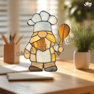 May include: Stained glass gnome chef figurine, wearing a white chef's hat and apron, holding a wooden spoon. The gnome's beard and body are shades of yellow and brown. The figurine is on a wooden surface.