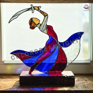 May include: Stained glass sculpture of a figure in a flowing dress, holding a sword aloft. The figure is in red, blue, and white glass, mounted on a dark wooden base. The text "ColorDreamLight" is visible.