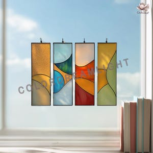 Pode incluir: Quatro painéis retangulares de vitrais com desenhos abstratos em tons de ouro, azul, verde, vermelho e amarelo. Cada painel é emoldurado em preto e pendurado por um pequeno gancho. O texto "COLOR DREAM LIGHT" é visível.