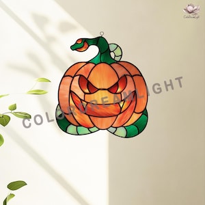Puede incluir: Decoración de calabaza de Halloween de vidriera con una cara amenazante. La calabaza es naranja con ojos rojos y una amplia sonrisa. Una vid verde con una serpiente se enrolla alrededor de la parte superior e inferior. Las palabras "COLOR DREAM LIGHT" son visibles.