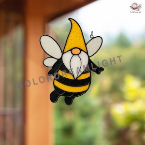 May include: A stained glass bee gnome with a yellow hat, black and yellow striped body, white beard, and white wings. The gnome has a small orange nose and is hanging from a hook. The words "COLOR DREAM LIGHT" are visible.