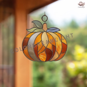 May include: Stained glass pumpkin decoration with orange, yellow, and brown segments. The pumpkin has a stem, leaves, and a metal ring for hanging. The design is reminiscent of fall and autumn decor.