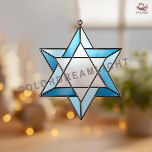 May include: A stained glass Star of David suncatcher with a metallic frame. The star features shades of blue and white glass, with a central silver-colored panel. The suncatcher is designed to hang and has a small loop at the top.