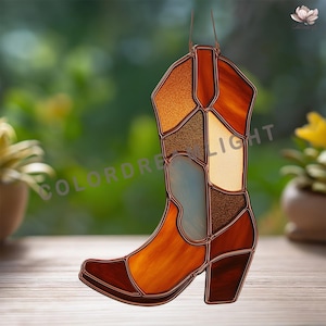 May include: A stained glass cowboy boot suncatcher in shades of brown, orange, and tan. The boot has a pointed toe, a heel, and a decorative design. The text "COLORDREAMLIGHT" is visible on the boot.