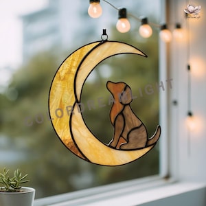 May include: Stained glass crescent moon with a brown dog silhouette. The moon is a warm yellow with a textured pattern, and the dog is sitting and looking up. A black metal loop is at the top for hanging.