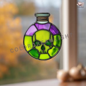 Può includere: Decorazione in vetro colorato a forma di bottiglia di pozione con un design a teschio. La bottiglia presenta un teschio verde, circondato da pannelli di vetro viola e verde. La bottiglia ha una parte superiore marrone e uno sfondo sfocato.