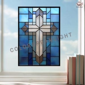 May include: Stained glass window featuring a white cross design with geometric blue and gray panels. The window is framed in black and has the text "COLOR DREAM LIGHT" on the lower left. A stack of books sits on the windowsill.