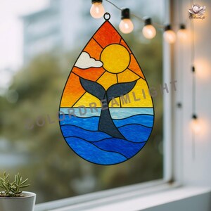 Peut inclure: Vitrail en forme de goutte d'eau représentant une queue de baleine dans l'océan sous un coucher de soleil. Le motif comprend un soleil jaune, un ciel orange et jaune et de l'eau bleue. Une pièce décorative pour fenêtre.