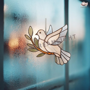 Può includere: Vetrata di una colomba con ramo d'ulivo, nei toni del bianco, crema e grigio. La colomba è sospesa da una catena, con la scritta "DREAM LIGHT" visibile. Il disegno è su uno sfondo sfocato blu.