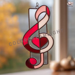 May include: Stained glass treble clef suncatcher with a heart design. The suncatcher features shades of red, pink, and white, with a silver-colored border. The words "COLOR DREAM LIGHT" are visible on the left side of the image.