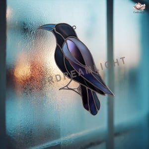 Peut inclure: Vitrail représentant un corbeau noir avec des ailes violettes et bleues et un bec bleu. Le corbeau est suspendu devant une fenêtre. Le capteur solaire a une boucle métallique pour l'accrocher. Le texte "Dream Light" est visible.