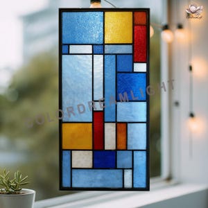 May include: A rectangular stained glass window with a black frame. The design features a geometric pattern of various colored glass panes, including blue, yellow, red, and white. The window is positioned in front of a window with a blurred background.